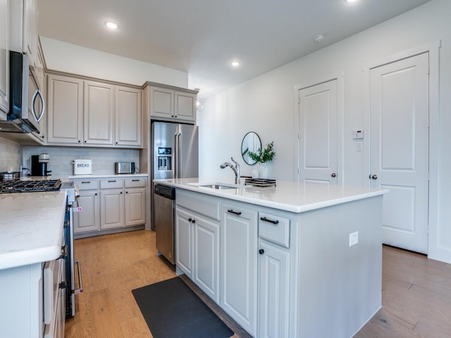 kitchen featuring sink, decorative backsplash, a center island with sink, appliances with stainless steel finishes, and light wood-type flooring