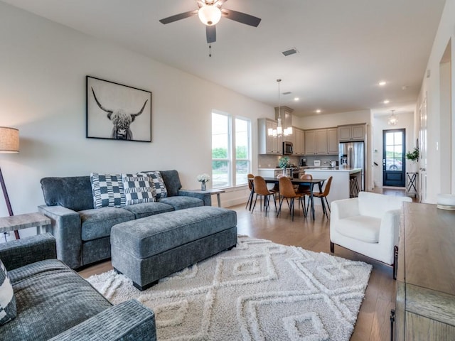 living room featuring ceiling fan with notable chandelier and light hardwood / wood-style flooring