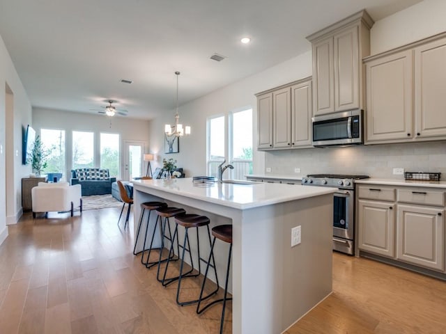 kitchen with stainless steel appliances, a wealth of natural light, a center island with sink, and light hardwood / wood-style floors