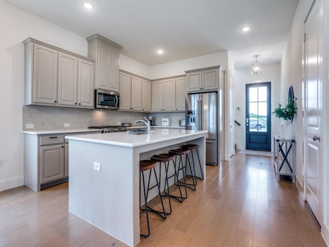 kitchen featuring appliances with stainless steel finishes, light wood-type flooring, a center island with sink, and a kitchen breakfast bar