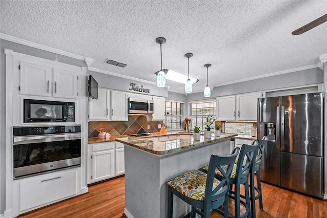 kitchen with white cabinetry, hanging light fixtures, wood-type flooring, a kitchen bar, and black appliances