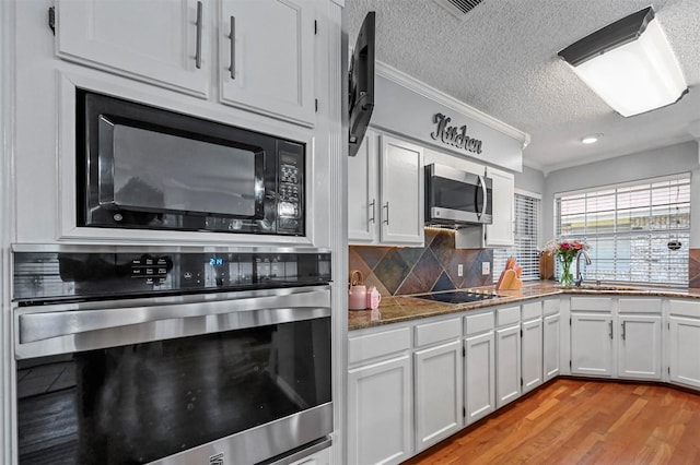 kitchen featuring white cabinetry, light hardwood / wood-style flooring, crown molding, a textured ceiling, and black appliances