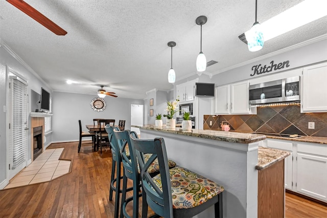 kitchen with a breakfast bar, hardwood / wood-style flooring, ceiling fan, decorative light fixtures, and white cabinetry