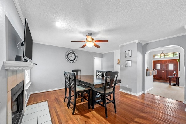 dining space featuring ceiling fan, wood-type flooring, a textured ceiling, a fireplace, and ornamental molding