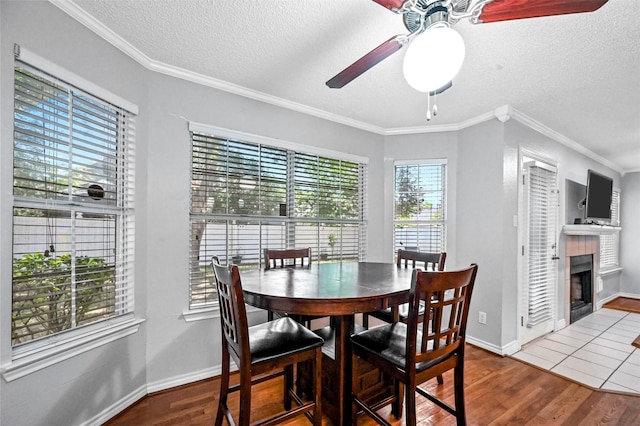 dining room with hardwood / wood-style floors, a wealth of natural light, ornamental molding, and a tiled fireplace