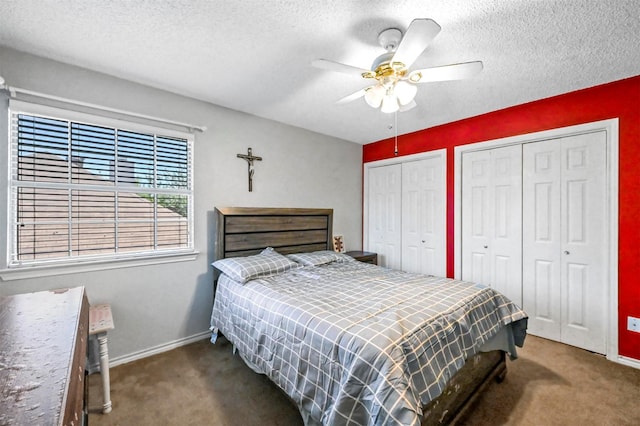 bedroom with ceiling fan, dark carpet, a textured ceiling, and multiple closets