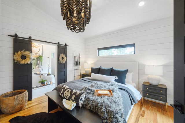 bedroom featuring a barn door, wood-type flooring, and lofted ceiling