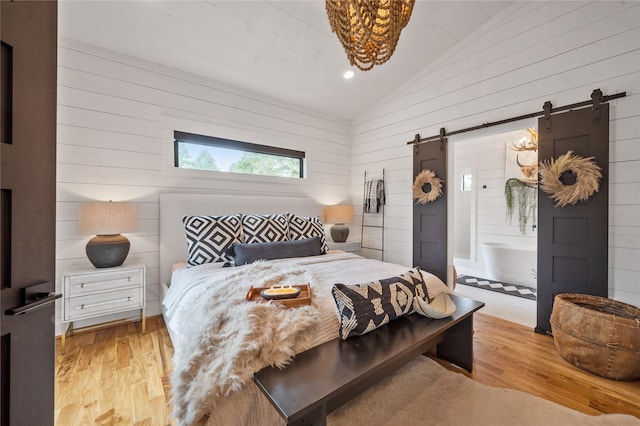 bedroom with light hardwood / wood-style flooring, vaulted ceiling, and a barn door