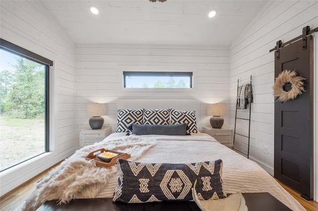 bedroom with multiple windows, a barn door, vaulted ceiling, and hardwood / wood-style flooring