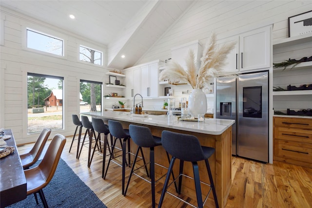 kitchen with a kitchen breakfast bar, a kitchen island with sink, high vaulted ceiling, white cabinets, and stainless steel fridge with ice dispenser