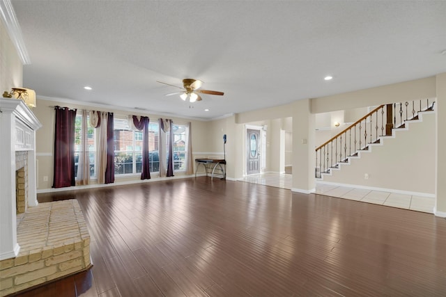 unfurnished living room featuring ceiling fan, ornamental molding, a textured ceiling, a fireplace, and wood-type flooring