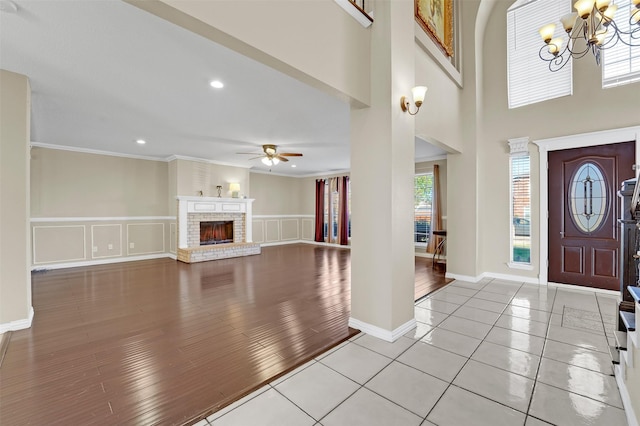 foyer featuring crown molding, light hardwood / wood-style floors, ceiling fan with notable chandelier, and a brick fireplace