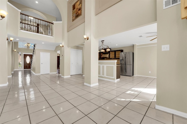 unfurnished living room featuring ceiling fan with notable chandelier, light tile patterned floors, and a towering ceiling