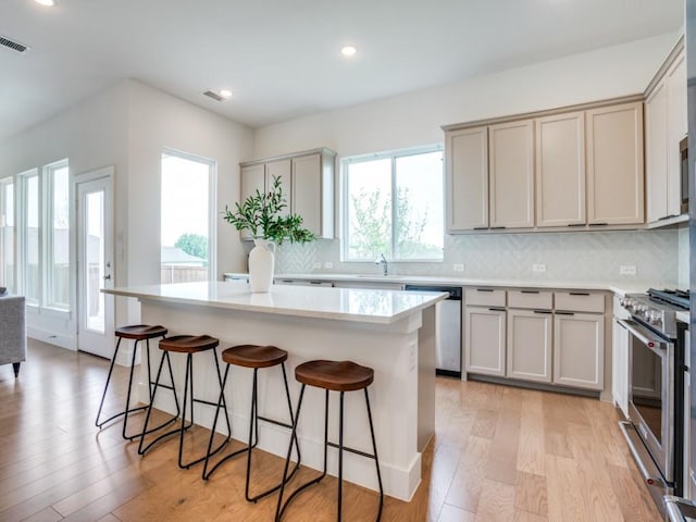 kitchen with a breakfast bar area, tasteful backsplash, a kitchen island, stainless steel appliances, and light hardwood / wood-style floors