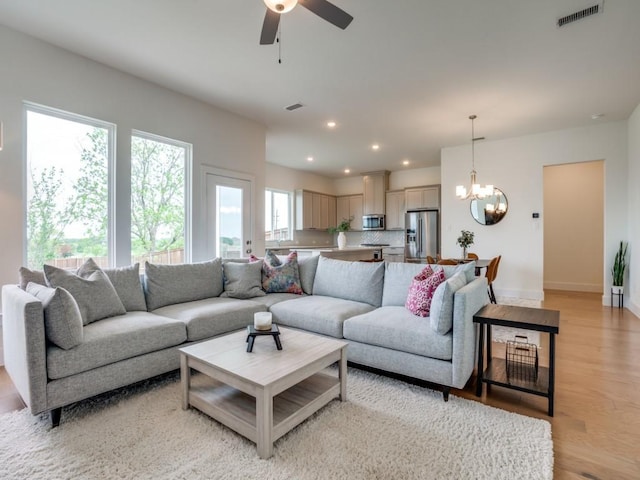 living room featuring ceiling fan with notable chandelier and light hardwood / wood-style floors