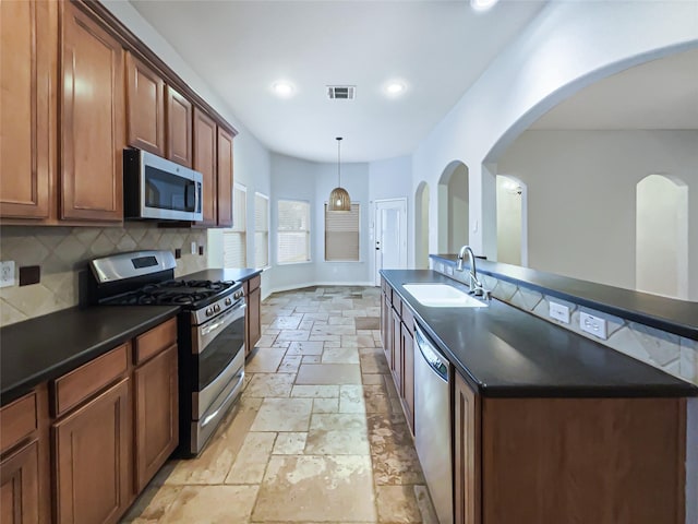 kitchen featuring pendant lighting, a center island with sink, sink, appliances with stainless steel finishes, and tasteful backsplash