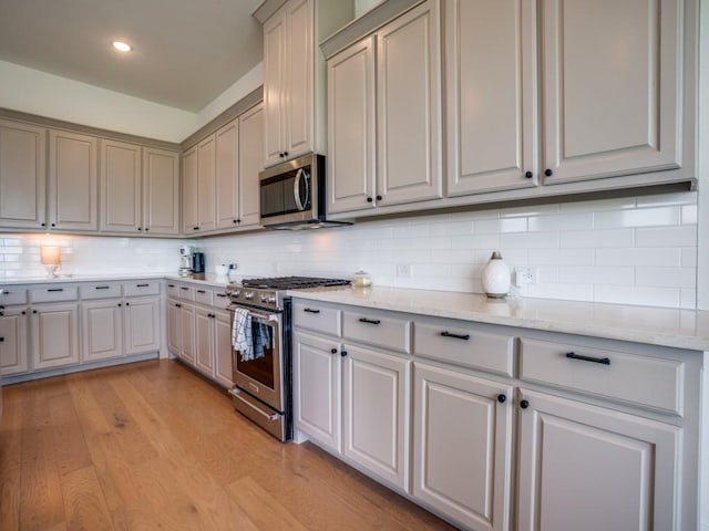 kitchen featuring decorative backsplash, appliances with stainless steel finishes, light hardwood / wood-style floors, and light stone countertops