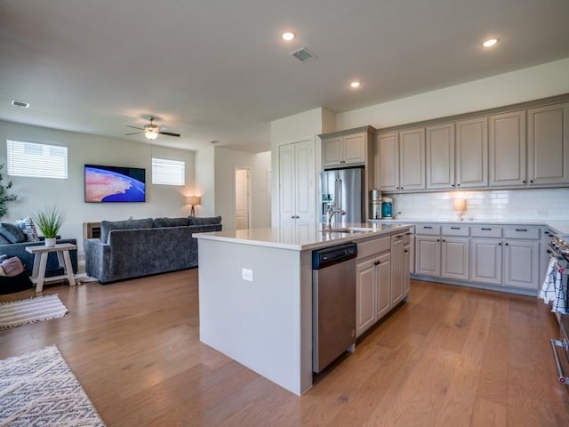 kitchen featuring tasteful backsplash, light hardwood / wood-style flooring, gray cabinets, a kitchen island with sink, and appliances with stainless steel finishes