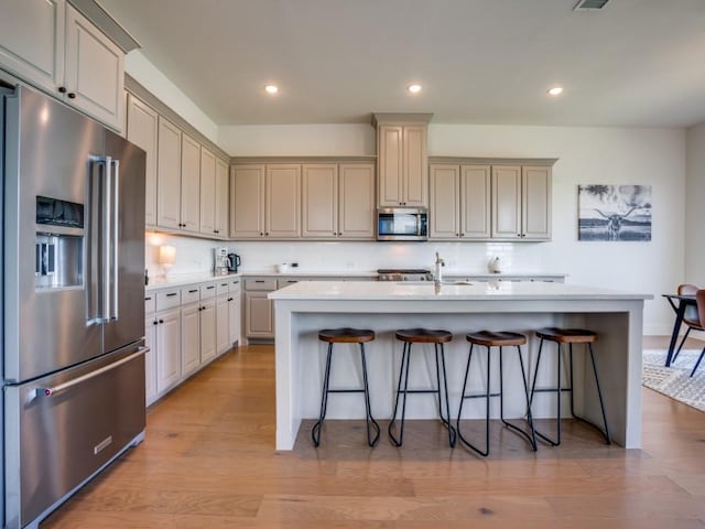 kitchen featuring sink, an island with sink, light hardwood / wood-style floors, a kitchen bar, and stainless steel appliances