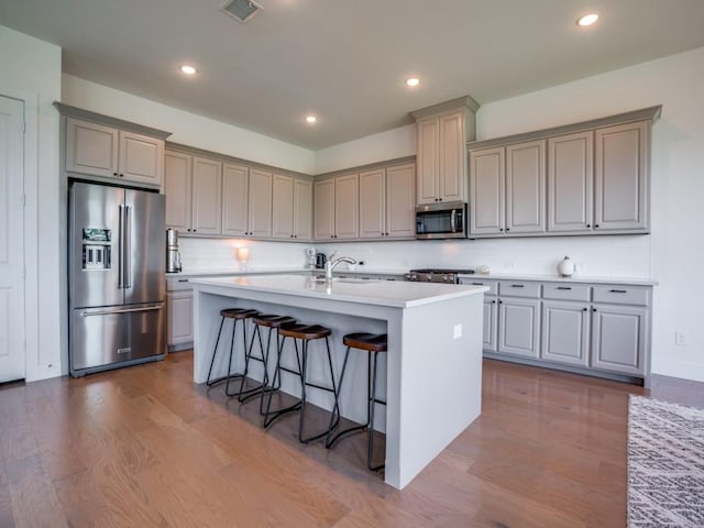 kitchen featuring hardwood / wood-style floors, a kitchen breakfast bar, decorative backsplash, an island with sink, and stainless steel appliances