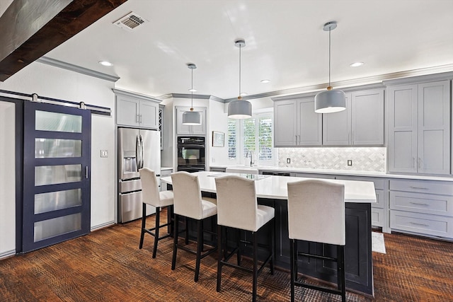 kitchen featuring a barn door, stainless steel refrigerator with ice dispenser, pendant lighting, gray cabinets, and a kitchen island