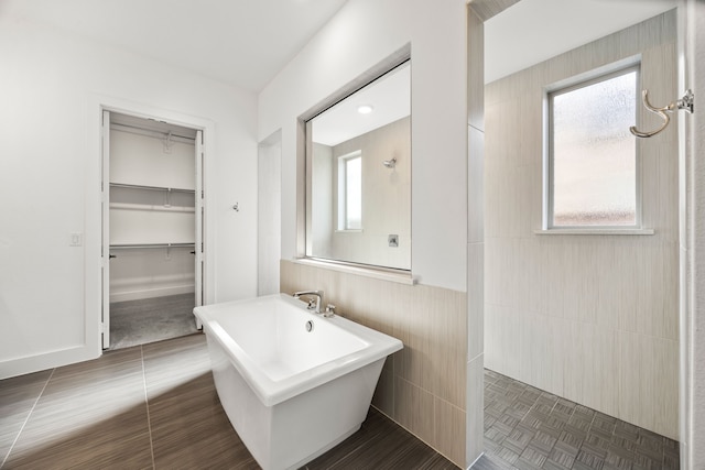 bathroom featuring tile patterned flooring, plenty of natural light, tile walls, and plus walk in shower