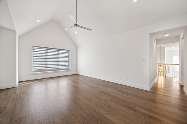 unfurnished living room with ceiling fan with notable chandelier, dark wood-type flooring, and high vaulted ceiling