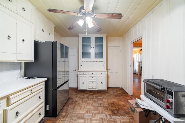 kitchen with dark parquet flooring, white cabinetry, ceiling fan, tasteful backsplash, and black fridge