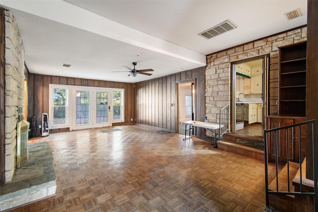 unfurnished living room with visible vents, wood walls, and a ceiling fan