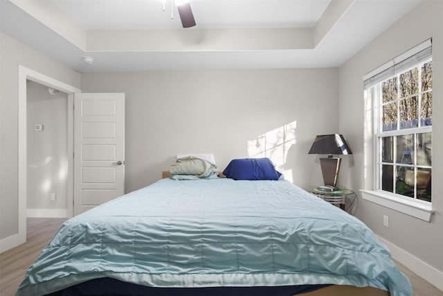 bedroom with ceiling fan, a raised ceiling, and hardwood / wood-style floors