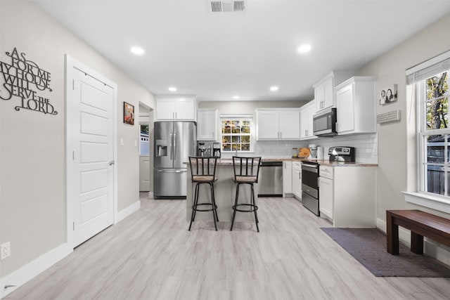 kitchen with white cabinets, light wood-type flooring, stainless steel appliances, and a wealth of natural light