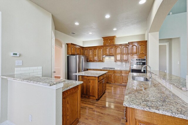 kitchen with kitchen peninsula, appliances with stainless steel finishes, backsplash, sink, and light hardwood / wood-style floors