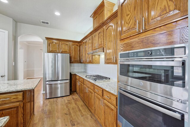 kitchen with decorative backsplash, appliances with stainless steel finishes, light hardwood / wood-style flooring, and light stone counters