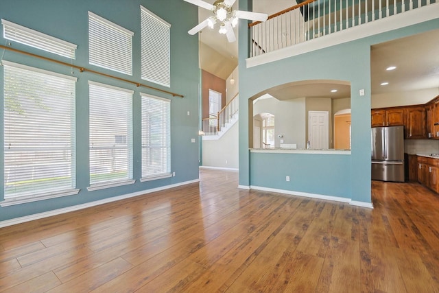 unfurnished living room with ceiling fan, hardwood / wood-style floors, and a high ceiling