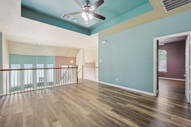 unfurnished room with ceiling fan, hardwood / wood-style floors, lofted ceiling, a textured ceiling, and a tray ceiling