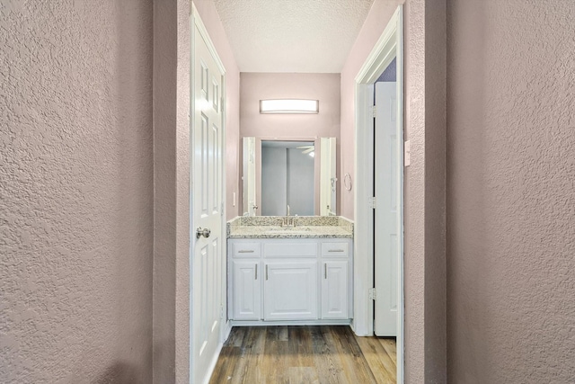 corridor with a textured ceiling, light wood-type flooring, and sink