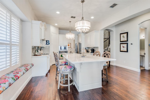 kitchen with appliances with stainless steel finishes, backsplash, white cabinets, dark hardwood / wood-style floors, and hanging light fixtures