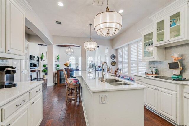 kitchen with pendant lighting, dark wood-type flooring, sink, an island with sink, and a chandelier