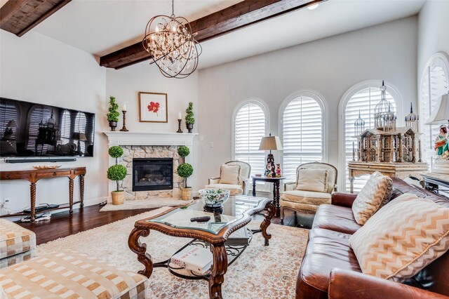 living room with hardwood / wood-style flooring, a notable chandelier, a stone fireplace, and beamed ceiling