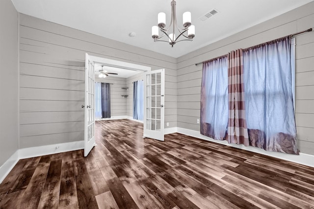 unfurnished dining area featuring french doors, ceiling fan with notable chandelier, wooden walls, and wood-type flooring