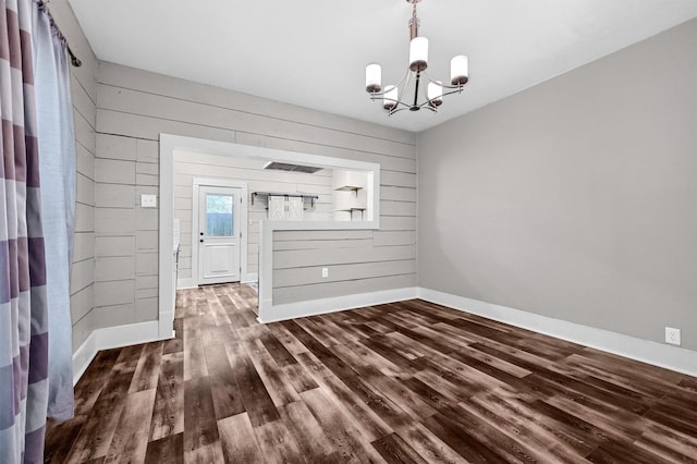 unfurnished dining area featuring wooden walls, dark hardwood / wood-style flooring, and a notable chandelier