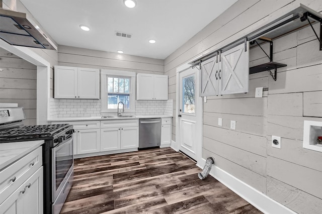 kitchen with wood walls, dark hardwood / wood-style flooring, white cabinetry, and stainless steel appliances