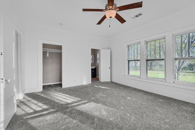 unfurnished bedroom featuring ensuite bath, dark carpet, ceiling fan, and ornamental molding