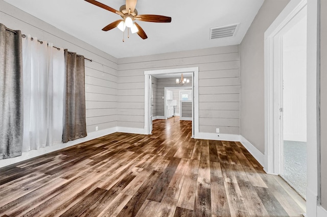 spare room featuring wooden walls, hardwood / wood-style floors, and ceiling fan with notable chandelier