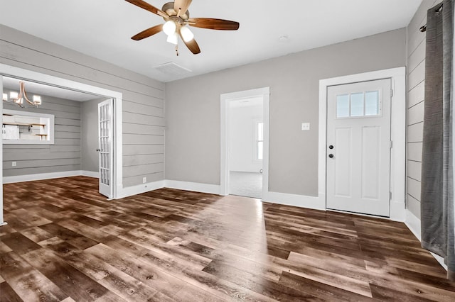 entrance foyer with ceiling fan with notable chandelier, dark wood-type flooring, and wooden walls