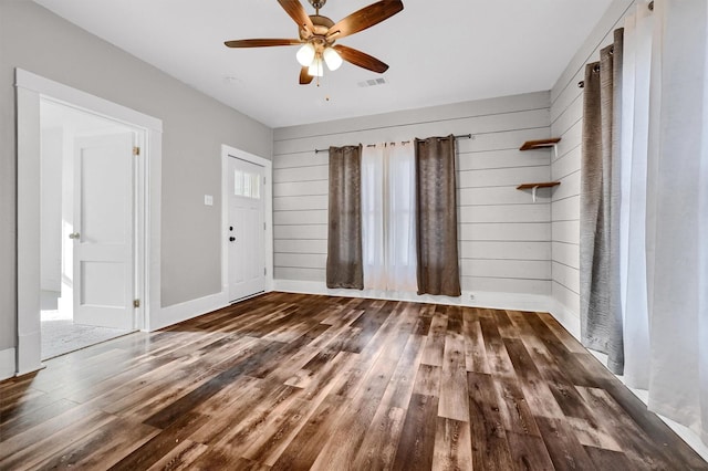 unfurnished room featuring wooden walls, ceiling fan, and dark wood-type flooring