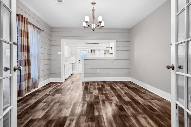 unfurnished dining area with wood walls, dark hardwood / wood-style flooring, a chandelier, and french doors