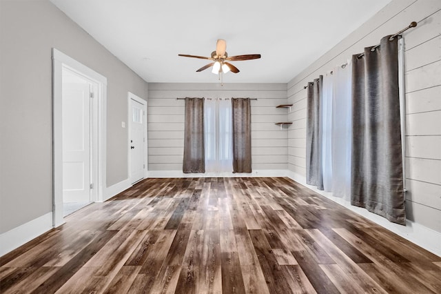 spare room with dark hardwood / wood-style floors, wood walls, and ceiling fan