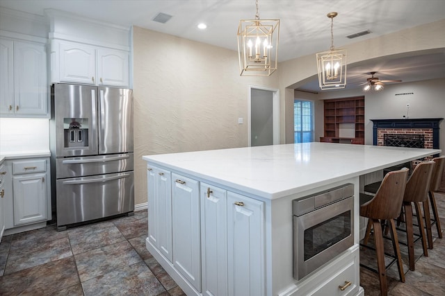 kitchen with appliances with stainless steel finishes, light stone counters, white cabinets, a kitchen island, and decorative light fixtures