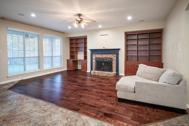 living room with a brick fireplace, ceiling fan, and built in shelves